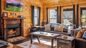 Ein gemütliches Blockhaus-Interieur mit Kamin, Ledersofa und großen Fenstern.