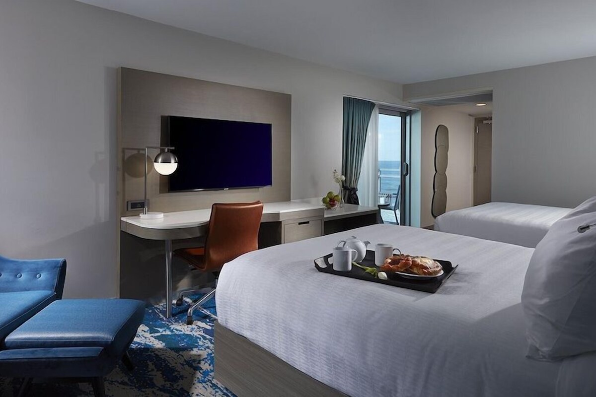 Une chambre d’hôtel avec un lit, un bureau, une chaise, une télévision et une vue sur l’océan.
