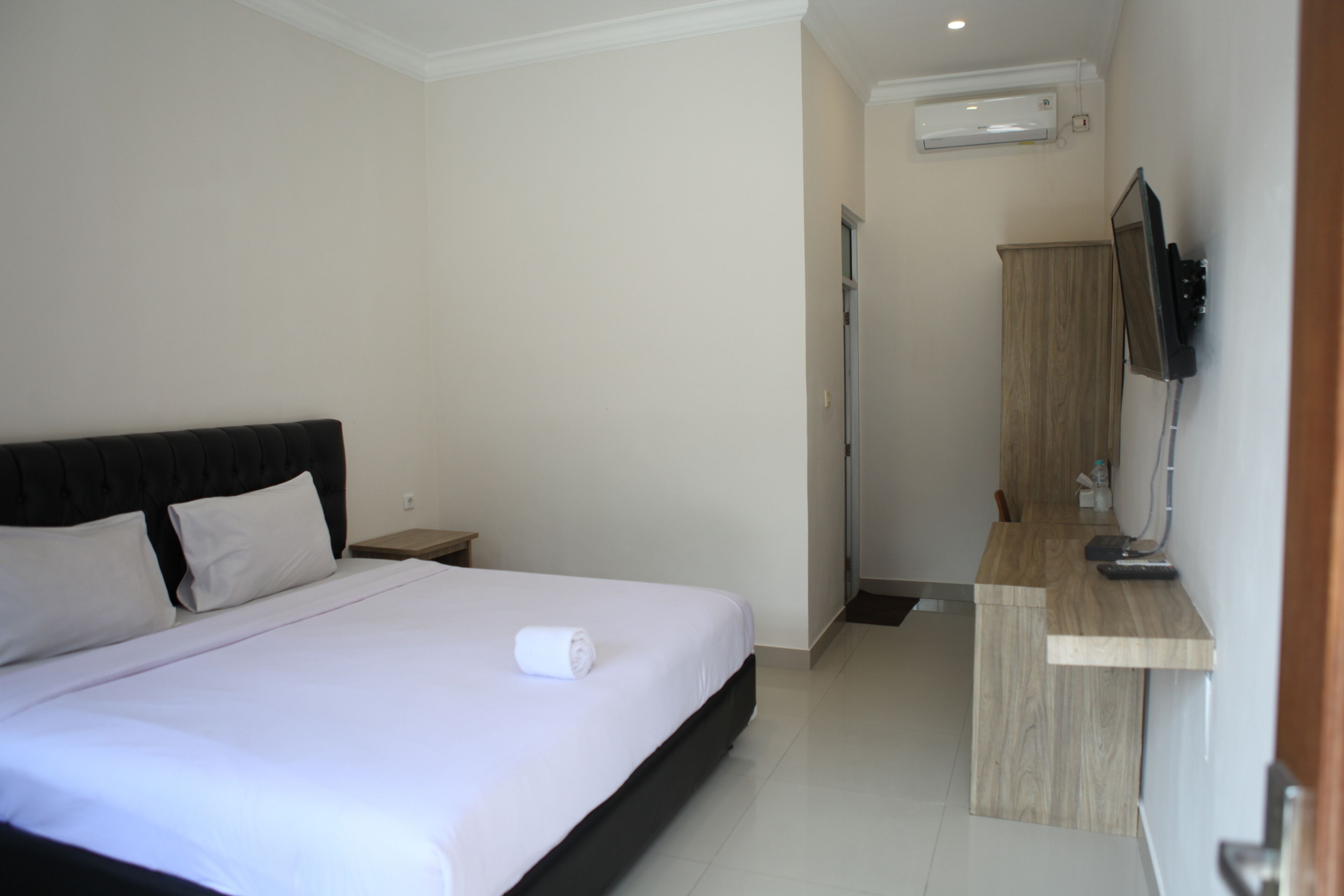 Una habitación de hotel con una cama, televisión, aparador de madera y unidad de aire acondicionado.