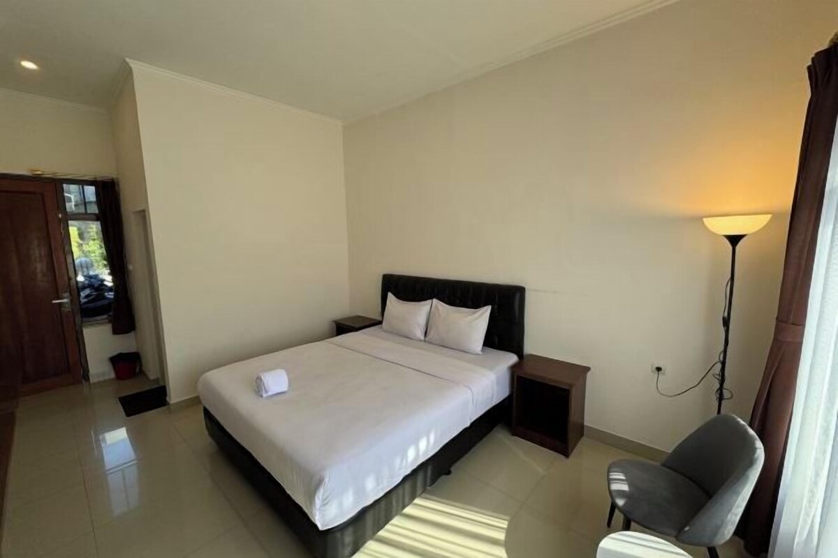 Une chambre à coucher comprenant un lit, une table de chevet, une chaise, une lampe et une porte donnant sur une autre pièce.