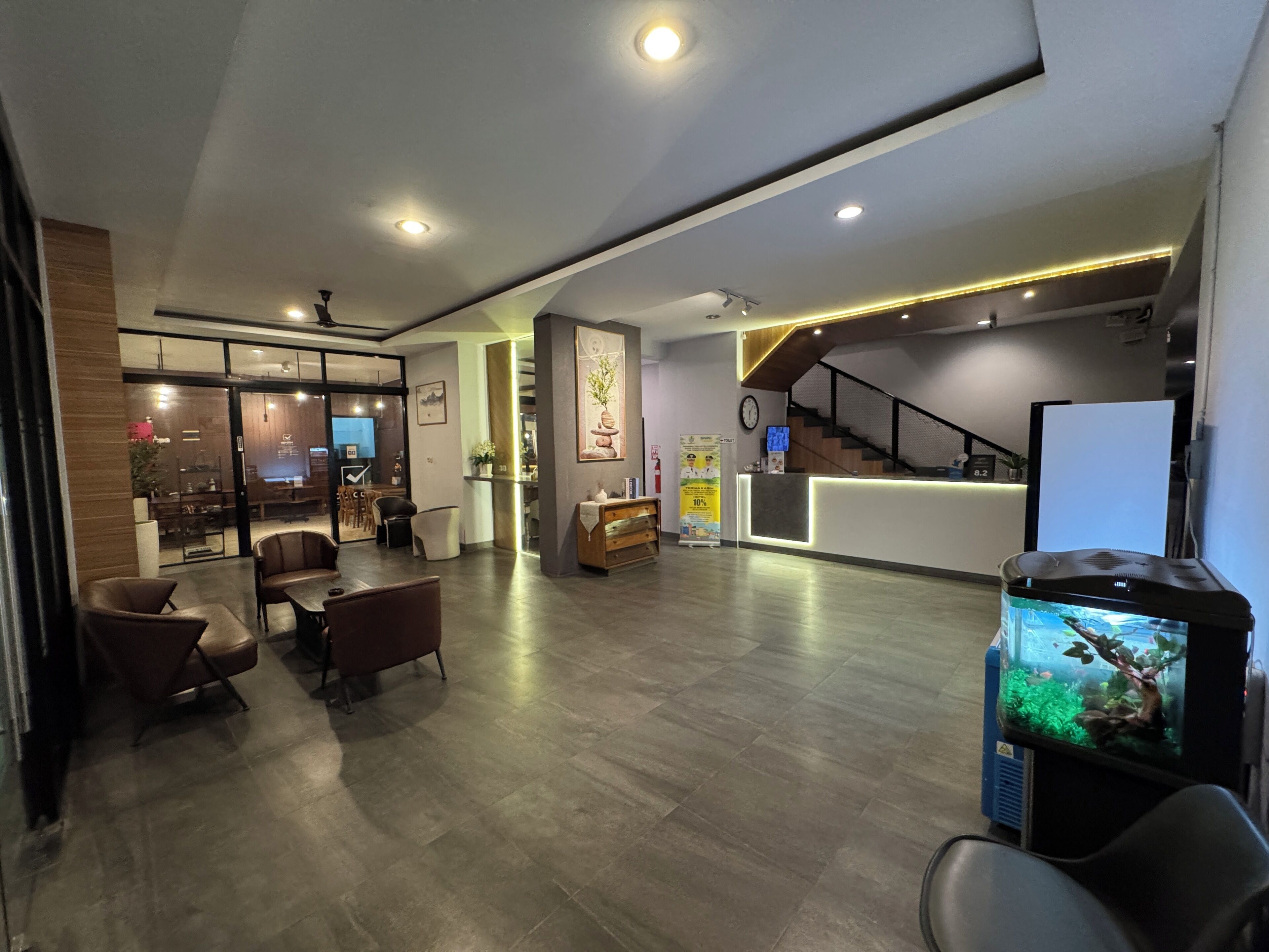 A modern hotel lobby with a reception desk, seating area, and a staircase.