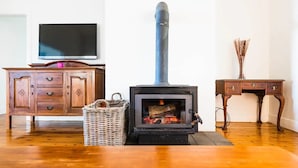 Une pièce avec un poêle à bois, une armoire en bois, un panier en osier et une petite table.