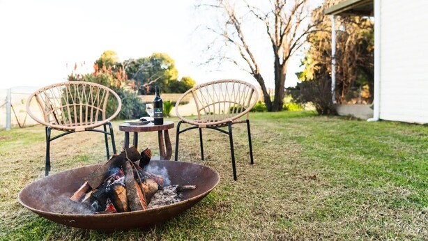 Un jardin avec un foyer, deux fauteuils en osier et une table sur laquelle se trouvent une bouteille et un verre.