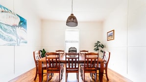Un coin repas avec une table et des chaises en bois, un luminaire suspendu et une fenêtre avec des stores.