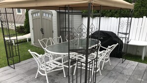 Katettu terassi, jossa on pyöreä pöytä ja valkoiset tuolit, grilli ja taustalla valkoinen aita.