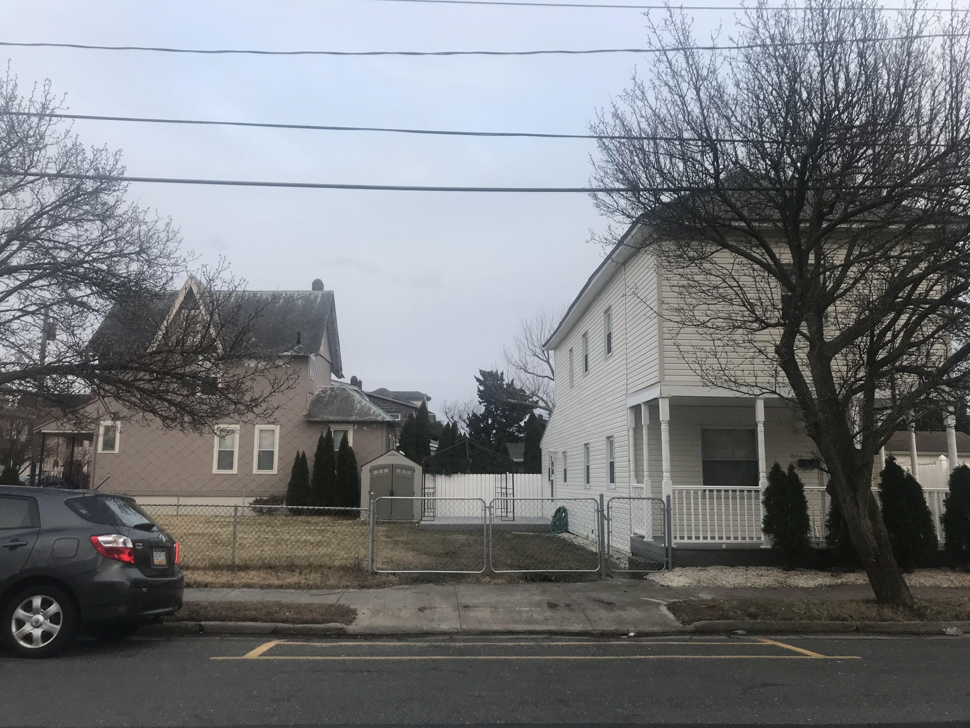 Une rue résidentielle bordée de maisons, avec une voiture garée et une zone délimitée par une grille.