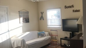 Une petite pièce bien éclairée, avec un lit simple, un téléviseur et un ventilateur de plafond.
