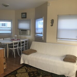 Ein gemütliches Wohnzimmer mit einem weißen Sofa, einem Esstisch mit Stühlen und einem gemusterten Teppich.