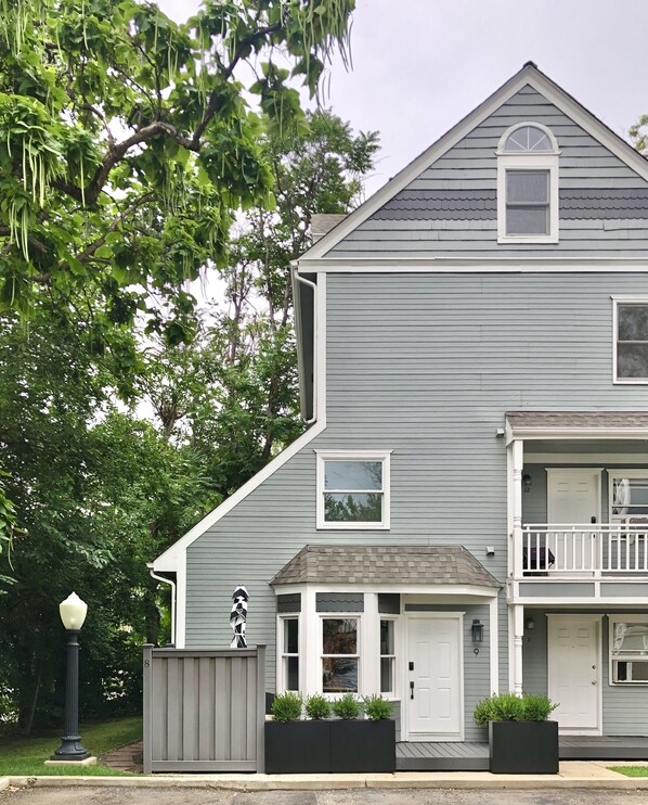 A two-story house with a grey exterior, a front porch, and a small balcony.