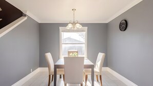 A dining area with a table and four chairs, a chandelier, a window with a view, and a clock on the wall. - Spacious 3 BR • Convenient • Big Yard • Office (Kyle)