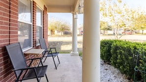 A covered outdoor seating area with brick walls, white columns, and a view of a parking lot and trees. - Spacious 3 BR • Convenient • Big Yard • Office (Kyle)