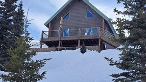 Una cabaña de madera con balcón, rodeada de árboles y nieve.