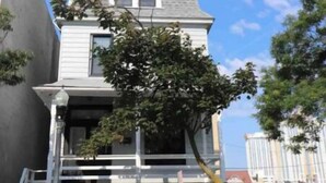 Un bâtiment à deux étages, avec un toit gris et des murs blancs, un arbre devant et deux voitures garées devant.