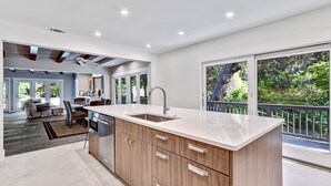 Een moderne keuken met een groot eiland, houten kastjes en uitzicht op weelderige begroeiing.