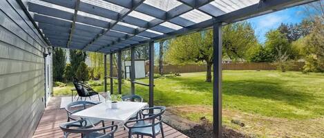 A covered patio with a table and chairs, a wooden deck, and a view of a grassy yard.