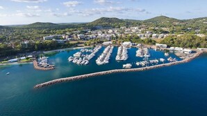 Une vue aérienne d’une marina où de nombreux bateaux sont amarrés, entourée de bâtiments résidentiels et avec des collines en arrière-plan.