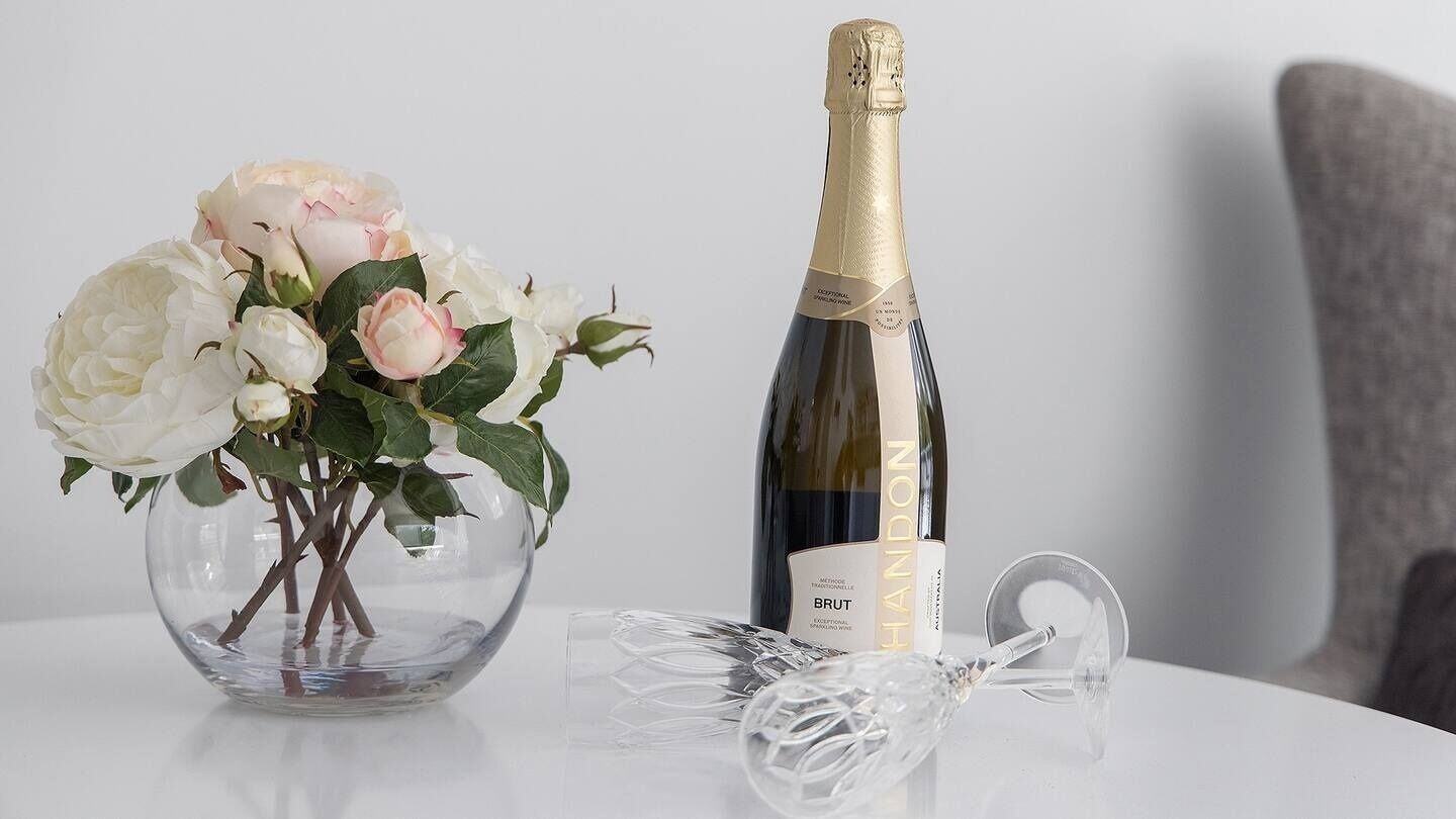 A bottle of Brut champagne, a glass, and a vase with flowers on a table.