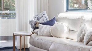 Un salon moderne avec un canapé blanc, une petite table ronde et une vue sur l’extérieur grâce à une grande fenêtre.