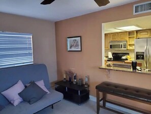 Relax in this stylish living space with a sofa, coffee table, and wooden bench, adjacent to a fully equipped kitchen.