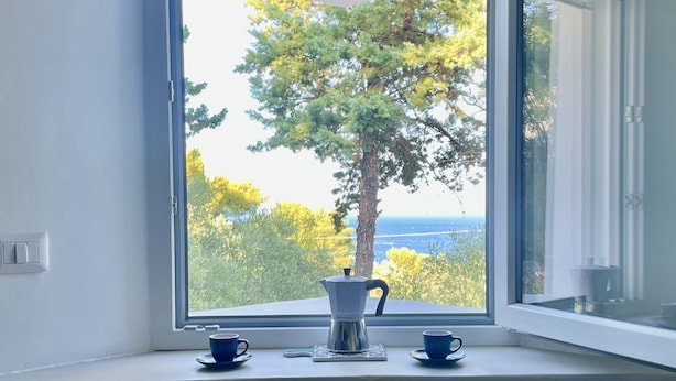 Une chambre moderne avec une grande fenêtre, une machine à café, deux tasses et deux chaises blanches.