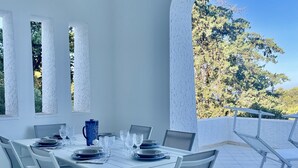 Un coin repas aux tons clairs, avec une table dressée pour six personnes, de grandes fenêtres et une vue sur les arbres.