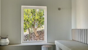 Une pièce au décor minimaliste, avec une grande fenêtre, un pouf rond et un canapé agrémenté de coussins à rayures.