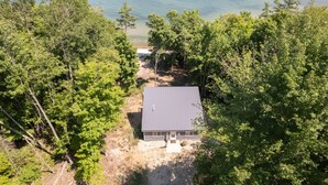 A single-story house with a dark roof, surrounded by dense green trees, near a body of water.