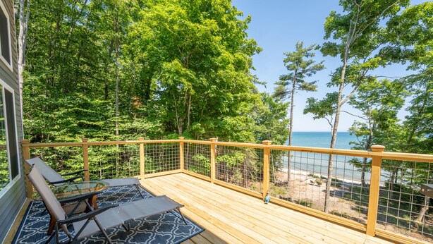 A wooden deck with a glass balustrade, a blue patterned rug, and two lounge chairs.
