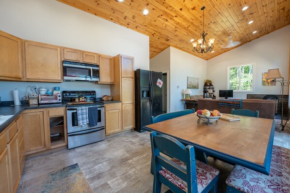 A kitchen with wooden cabinets, a stainless steel oven, and a refrigerator. There is a dining table with chairs and a chandelier above.