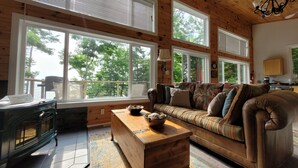 A cozy living room with a wooden ceiling, large windows, a sofa, a coffee table, and a fireplace.