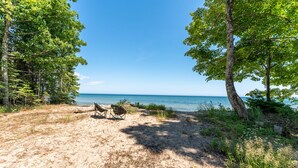 A beach with two chairs and a log, surrounded by trees and a clear view of the ocean.