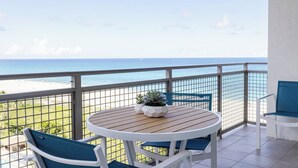 Un balcón con mesa y dos sillas de madera, con vista a la playa.