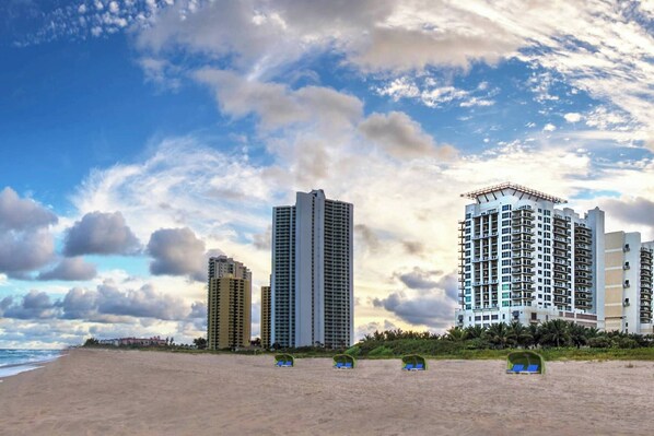 A beach with high-rise buildings in the background and beach umbrellas in the foreground. - Marriott Oceana Palms - Luxurious 2-Bedoom - Beachfront resort - Family Friendly (Riviera Beach)