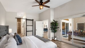Ein geräumiges Schlafzimmer mit einem großen Bett, einem Deckenventilator und einer Glastür, die in einen Wohnbereich mit einem Tischfußballspiel führt.