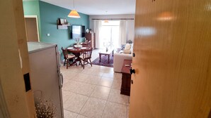 A living room with a dining area, a TV mounted on the wall, and a door with the number 106. - Dock Holiday Pool Apartment (Larnaca)