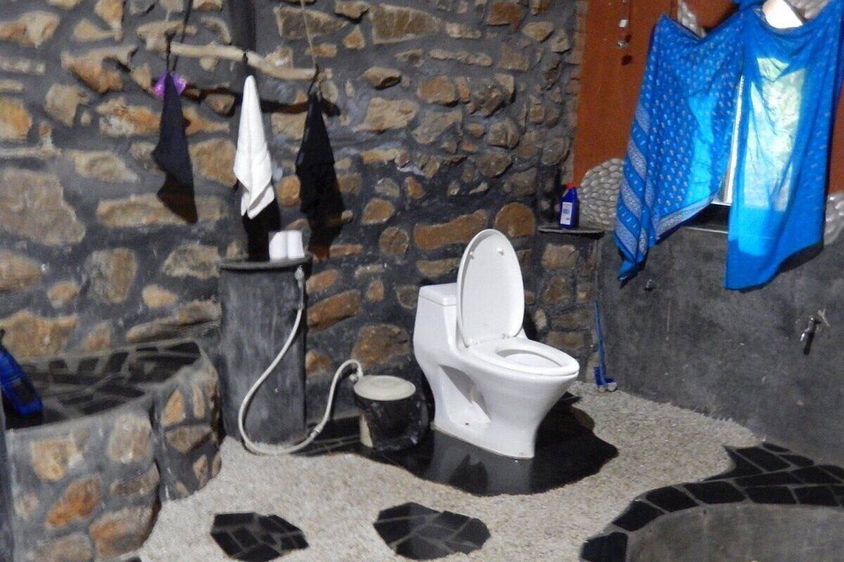 Een badkamer met een stenen muur, een wit toilet, een klein wastafeltje en een betegelde vloer.