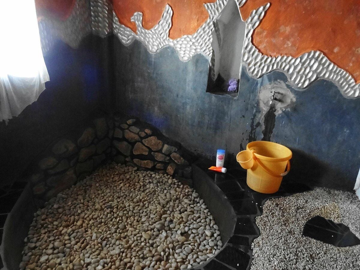 Quarto com parede de pedra, chão de pedriscos e uma banheira pequena cheia de pedrinhas.