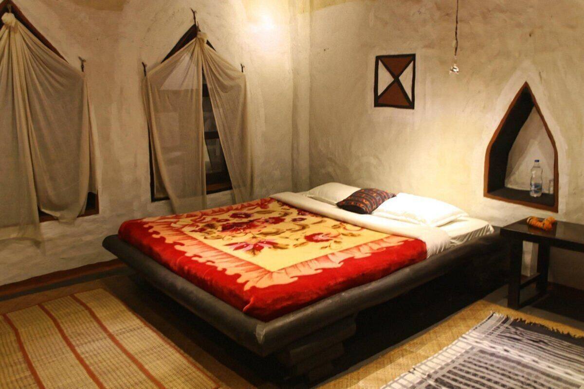 Een slaapkamer met een bed, nachtkastje, wandplank en een raam met gordijnen.