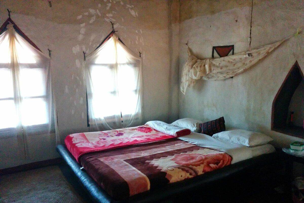 Een kamer met een bed, twee ramen voorzien van gordijnen en een decoratie aan de muur.