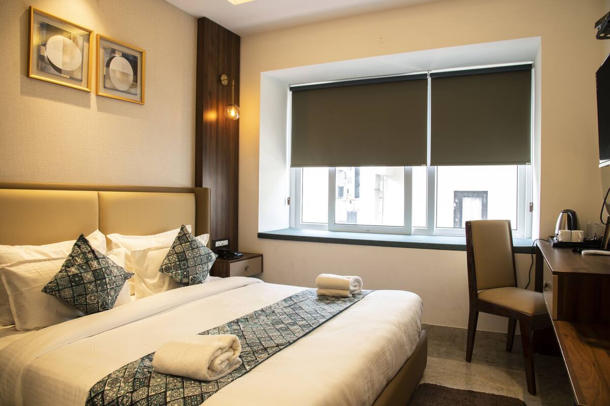 Une chambre d’hôtel avec un grand lit, un bureau, une chaise, une fenêtre donnant sur un beau paysage et deux tableaux encadrés accrochés au mur.