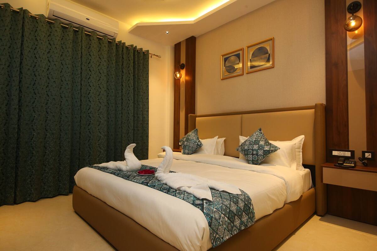 Une chambre d’hôtel avec un grand lit, une table de chevet, un climatiseur fixé au mur et une fenêtre avec des rideaux.