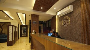 A hotel reception area with a wooden reception desk, a reception sign, and a wall-mounted air conditioning unit. - Hotel Dream Inn (Narendranagar)