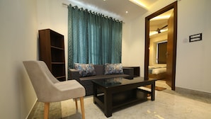 A living room with a sofa, a coffee table, and a chair. There is a bookshelf and a curtain. - Hotel Dream Inn (Narendranagar)