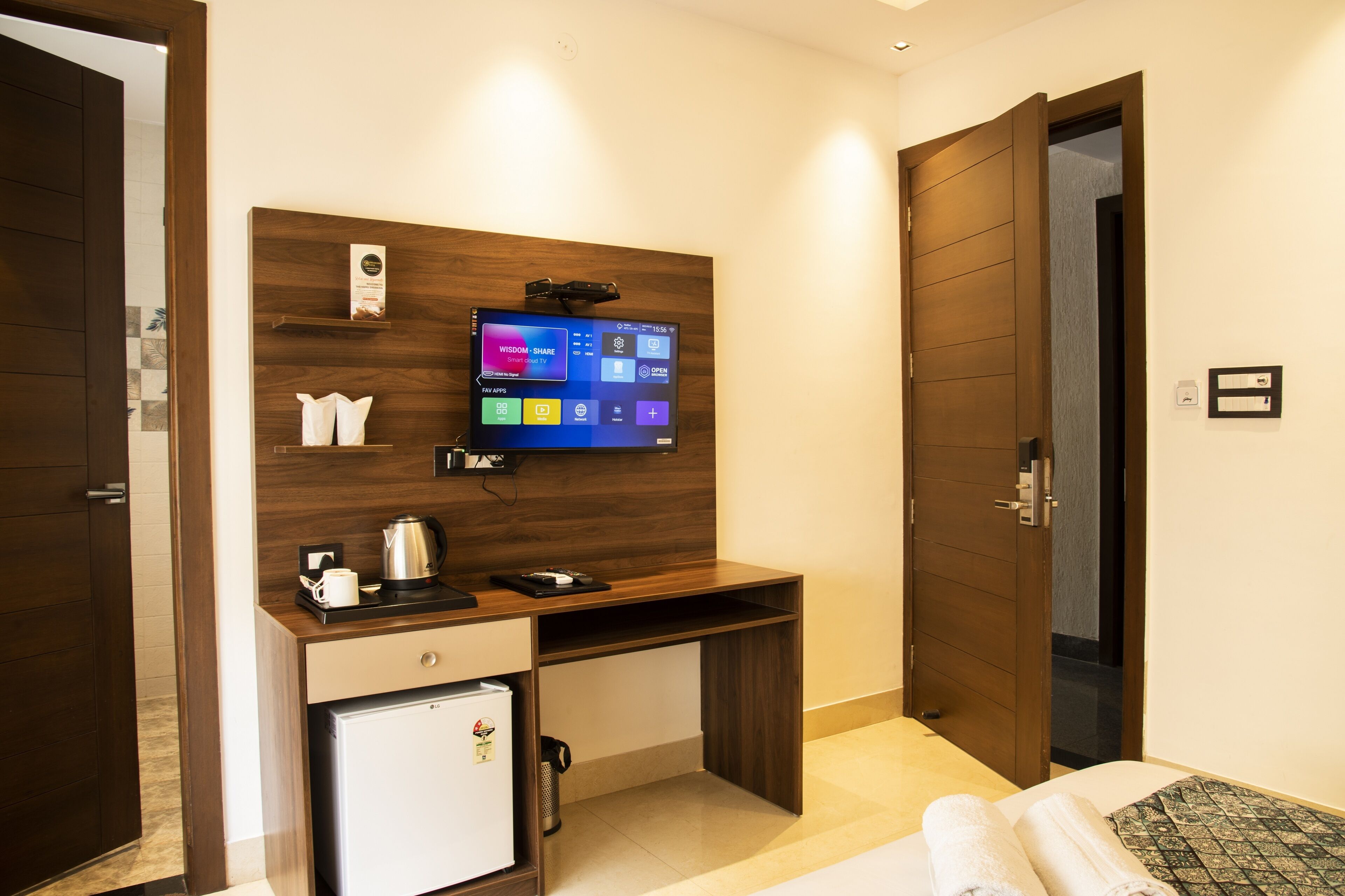 Habitación de hotel con escritorio de madera, televisor montado en la pared, refrigerador pequeño y cama con manta estampada.