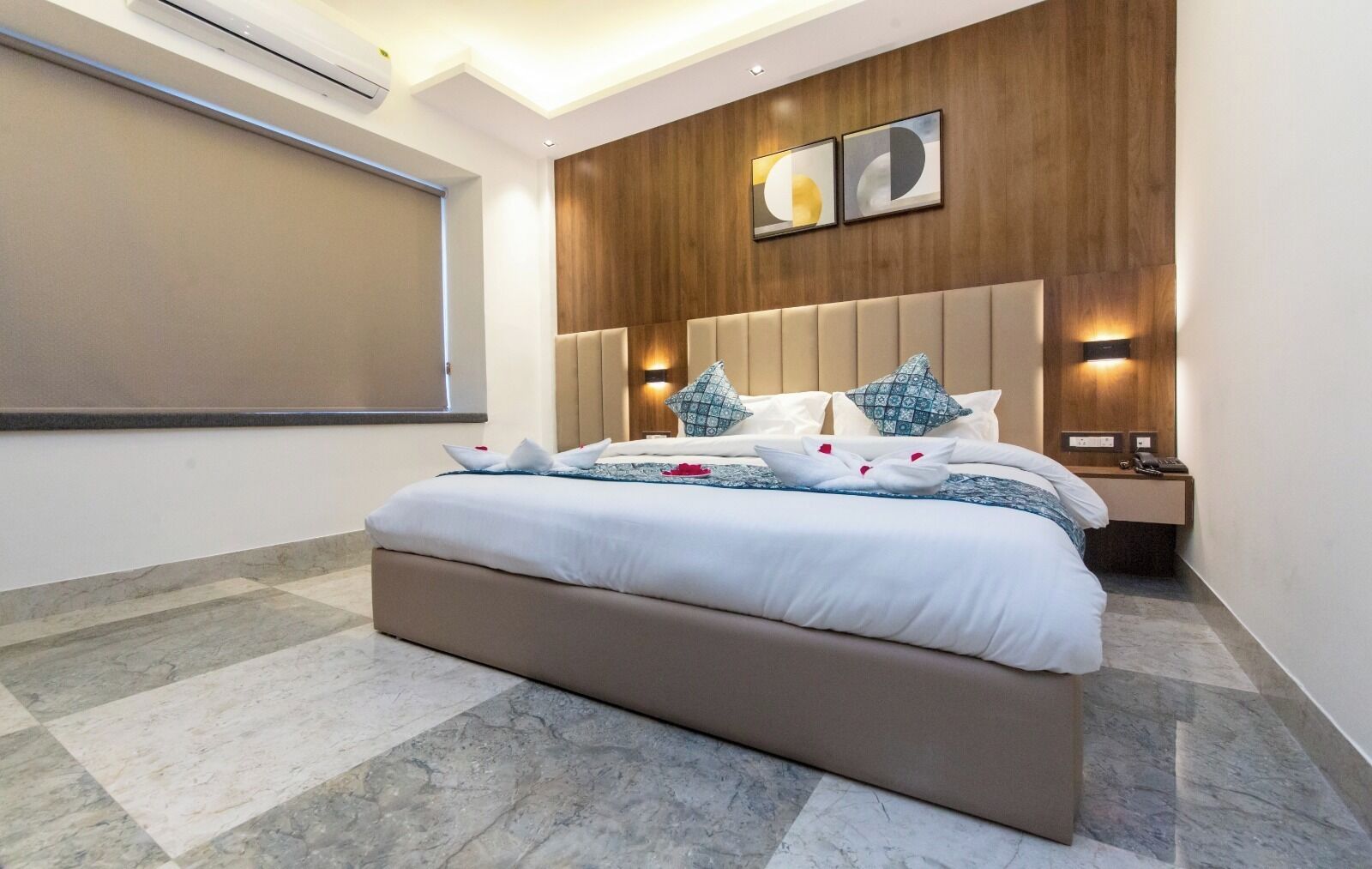 A modern bedroom with a large bed, wooden headboard, two bedside tables with lamps, and a large window.