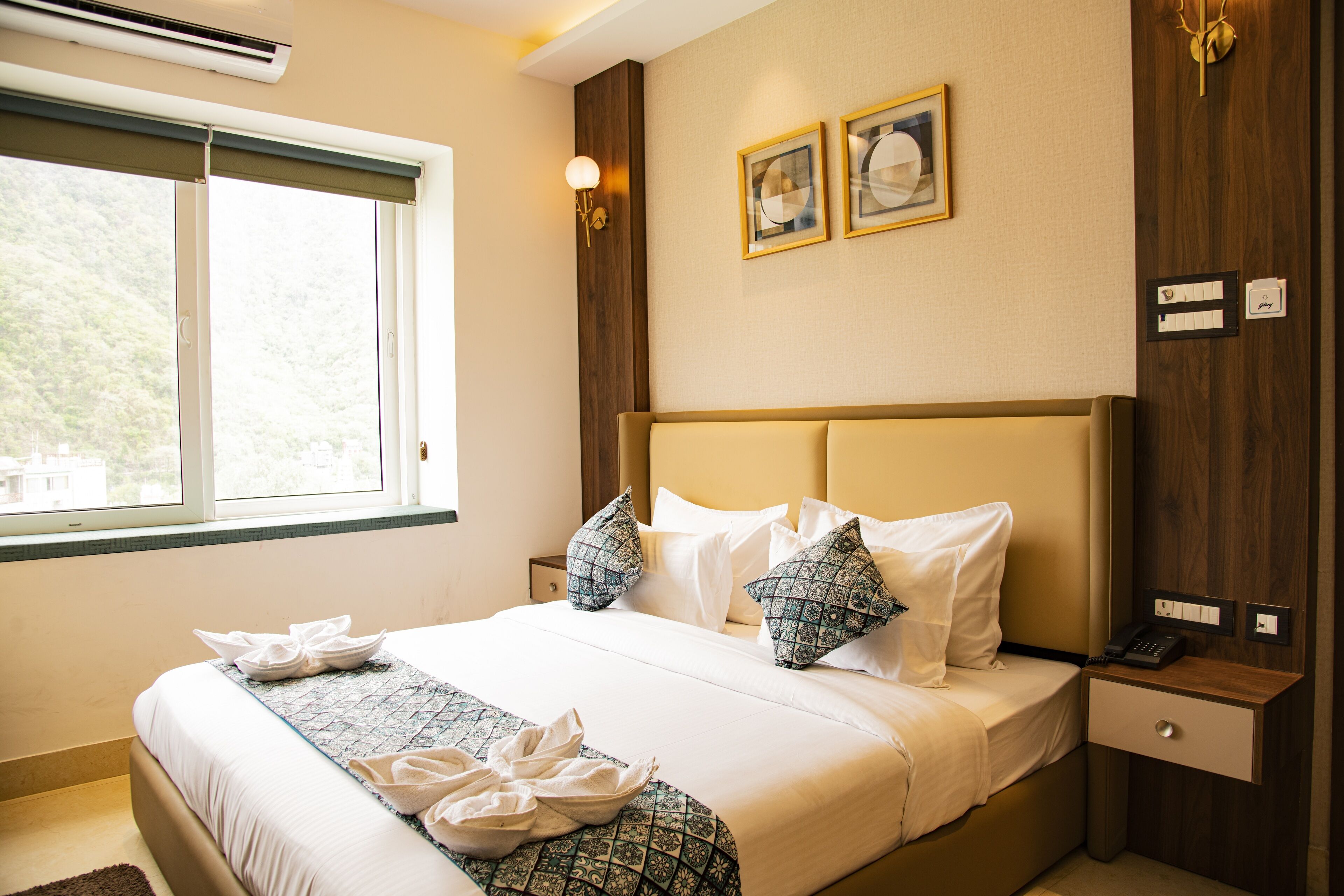 A neatly made bed with pillows, a bedside table with a phone, and a window with a view of greenery.