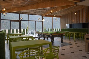 Una sala de billar con mesas y sillas, ventanas amplias y una mesa de billar.