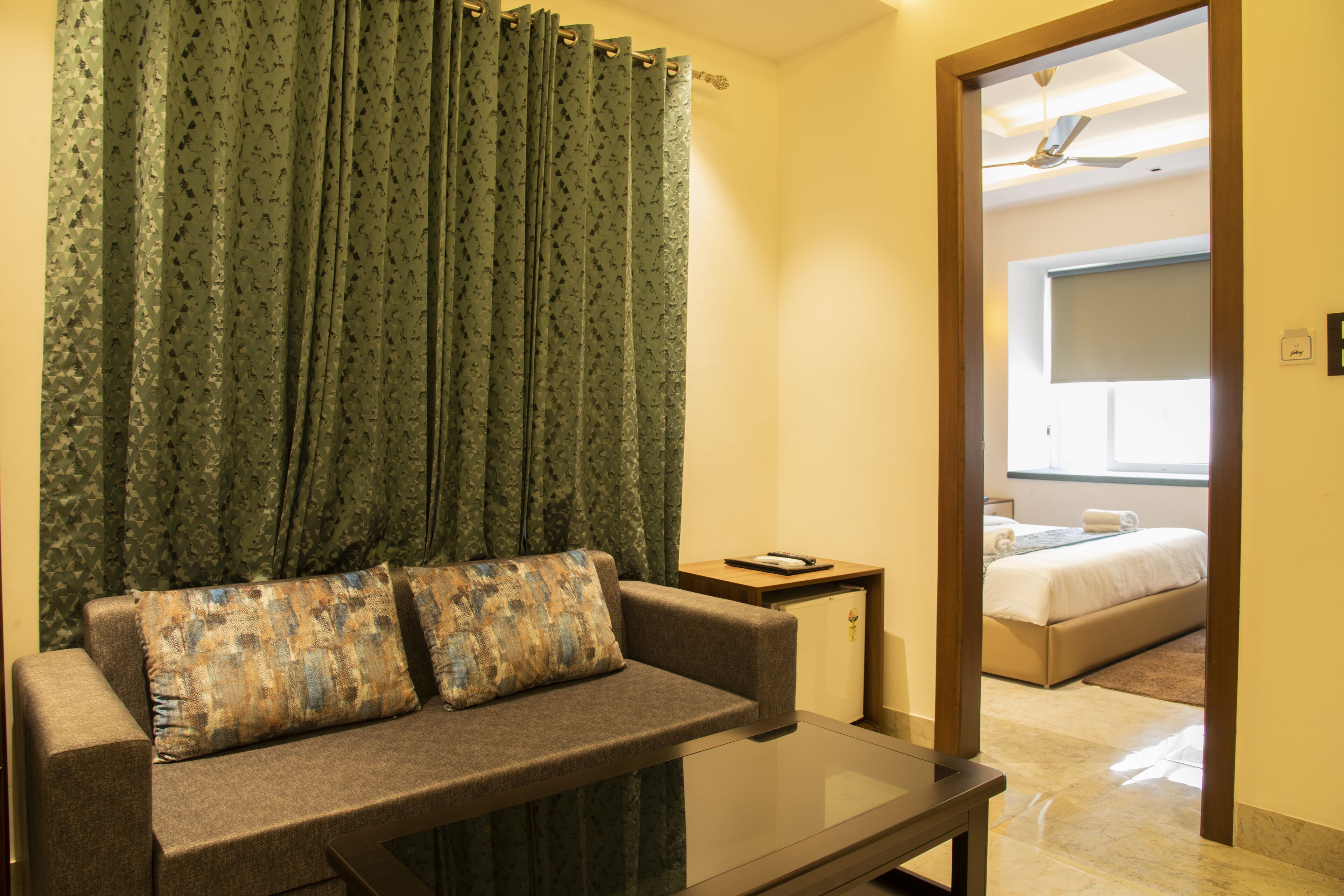 A room with a sofa, a small table, and a view into a bedroom with a bed and a ceiling fan.