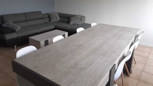 Una sala de estar con un sofá seccional gris, una mesita de centro pequeña y una mesa de comedor con sillas.