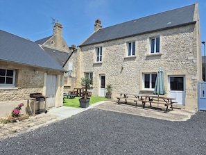 Un bâtiment en pierre avec une allée en gravier, un banc en bois et une table de pique-nique.